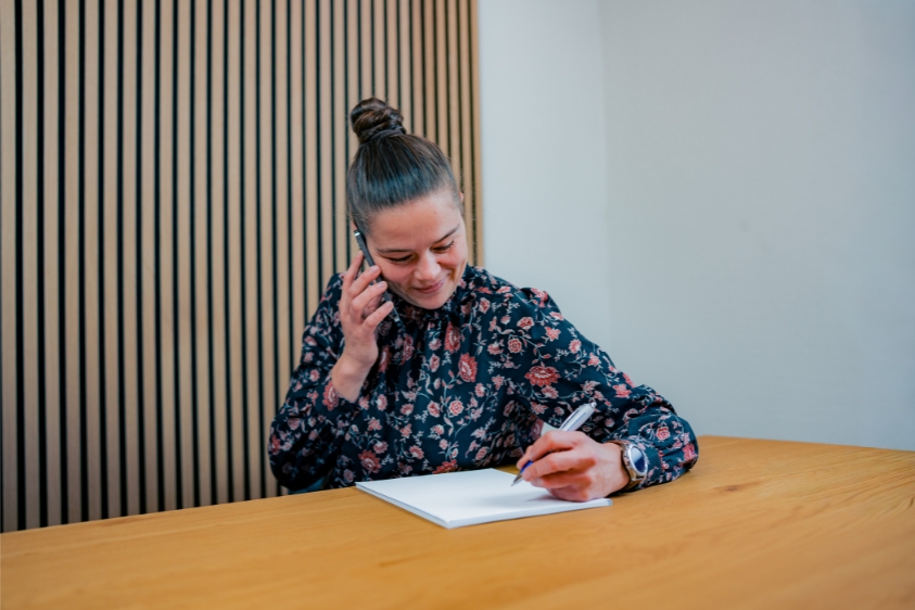 Mitarbeiterin telefoniert und macht sich Notizen am Schreibtisch