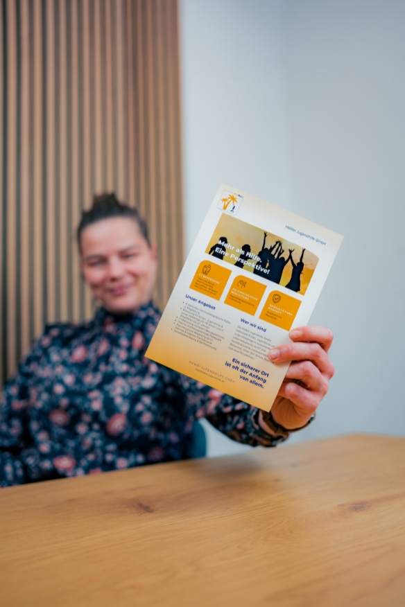Mitarbeiterin präsentiert HaWei Jugendhilfe Flyer mit einem Lächeln